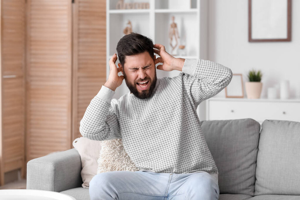 Angry young man suffering from loud noise at home - Foto, afbeelding