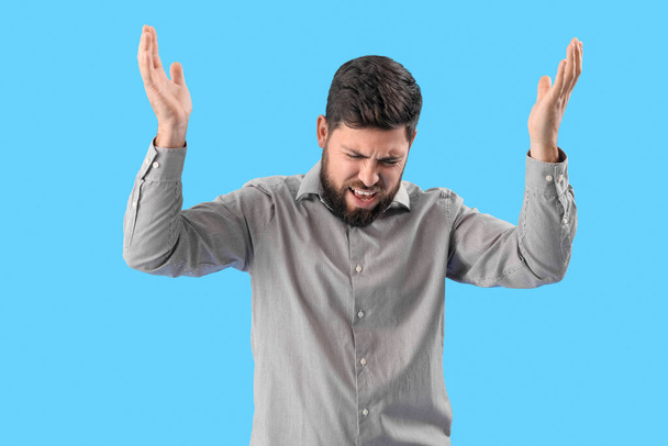 Stressed young man suffering from loud noise on blue background - Photo, image