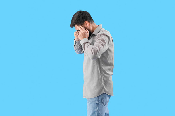 Young man suffering from loud noise on blue background - Φωτογραφία, εικόνα