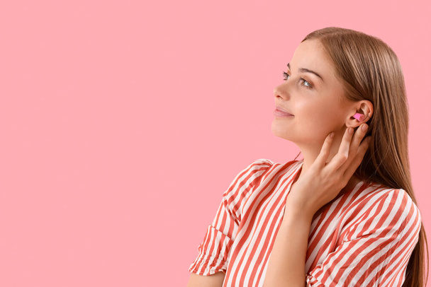 Young woman with ear plugs on pink background, closeup - Фото, изображение