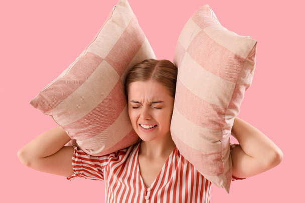 Молодая женщина с подушками страдает от громкого шума на розовом фоне, крупным планом - Фото, изображение