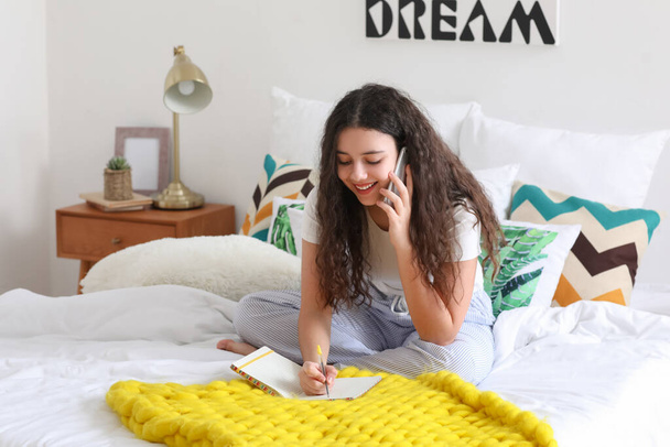 Teenagermädchen mit Notizbuch telefoniert im Schlafzimmer - Foto, Bild