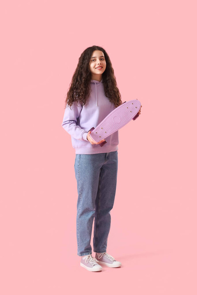 Chica adolescente con monopatín sobre fondo rosa - Foto, imagen