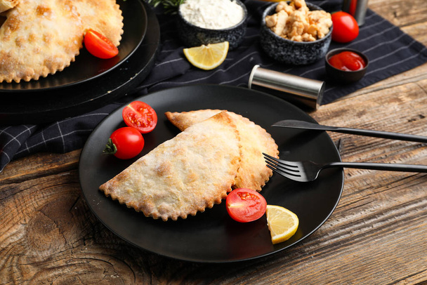 Platen met gebakken vlees empanadas en tomaten op houten tafel, close-up - Foto, afbeelding