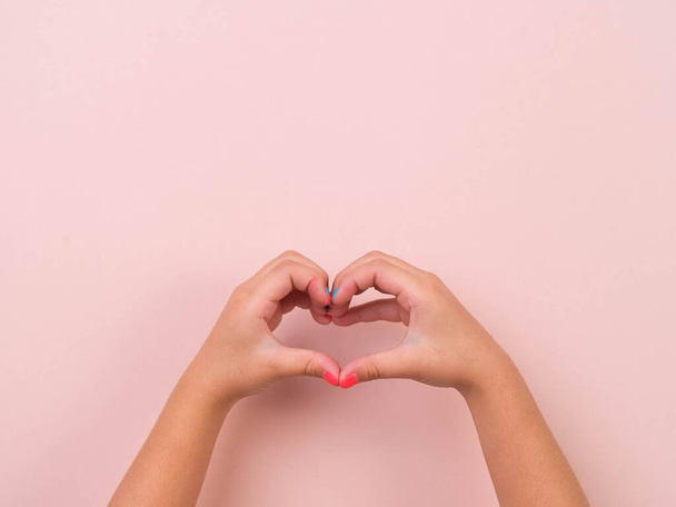 Dívka ruka ukazuje tvar srdce, lásku a sympatie symbol na růžovém pozadí ve studiu. Smečka pohybů a řeči těla. - Fotografie, Obrázek