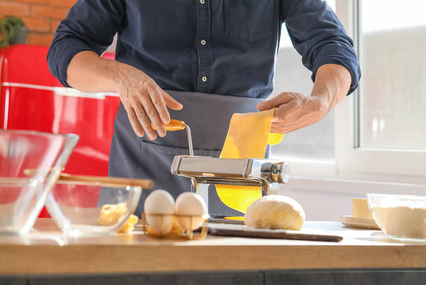 Man making pasta with machine at table in kitchen, closeup - Photo, Image