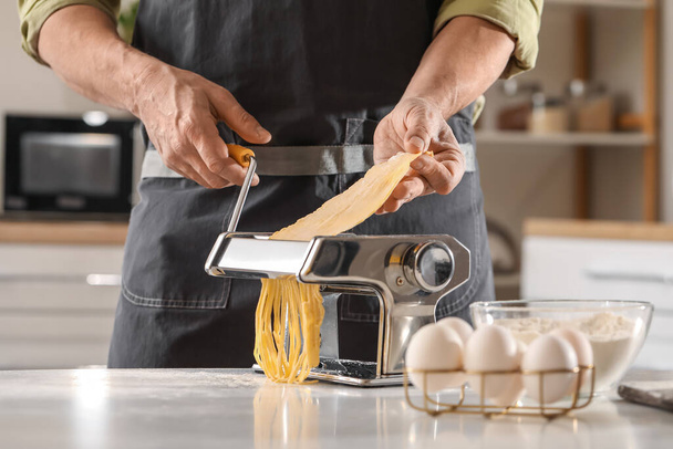 Man making pasta with machine at table in kitchen, closeup - Φωτογραφία, εικόνα