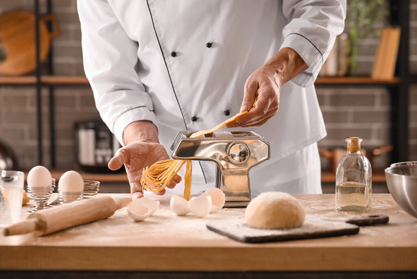 Мужчина шеф-повар делает макароны с машиной за столом на кухне, крупный план - Фото, изображение