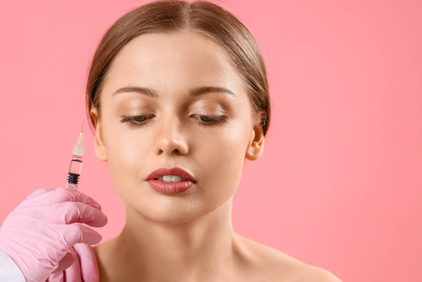 Jeune femme recevant l'injection de charge dans le visage sur fond rose - Photo, image