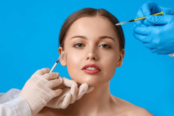 Молодая женщина получает инъекции наполнителя в лицо на синем фоне - Фото, изображение