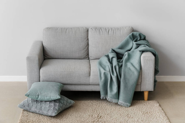Cozy sofa with cushions and plaid near grey wall - 写真・画像