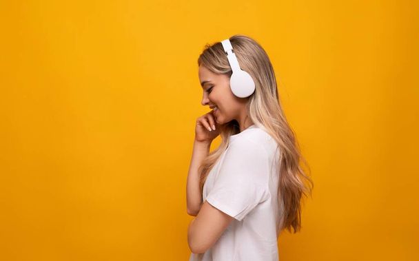μισογυρισμένο κορίτσι με άσπρα ακουστικά σε κίτρινο φόντο με κενό χώρο. - Φωτογραφία, εικόνα