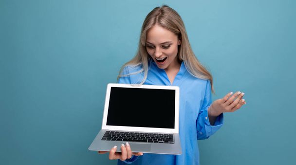 szczęśliwy szczęśliwy szczęśliwy blondynka dziewczyna miło zaskoczony z laptopem w jej rękach z puste miejsce na stronie internetowej na niebieskim tle. - Zdjęcie, obraz