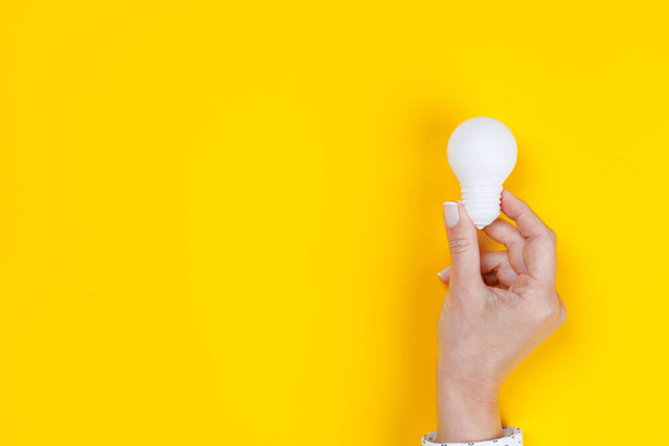 Woman hand holding a white light bulb on yellow background - Φωτογραφία, εικόνα