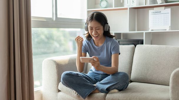 Woman playing games on mobile phone, Rejoices in victory, Female enjoying playing online games, Entertainment  or technology game trends, Weekend getaways in the living room at home. - Fotografie, Obrázek
