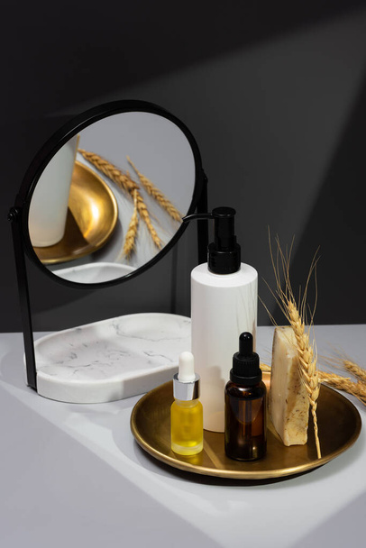 Set of essential oils, handmade soap and mirror on a dark gray background. Creative still life with organic cosmetics. The concept of selfcare and organic products. Reflection in the mirror. - Photo, Image