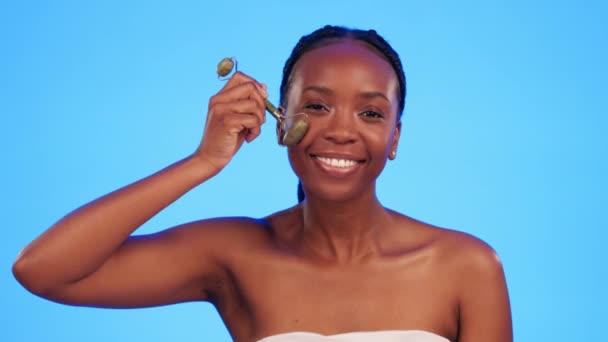 Jade roller, skincare and face of black woman in studio for wellness, anti aging and cosmetics on blue background. Portrait, massage and tool for girl model with luxury, beauty or lymphatic treatment. - Záběry, video
