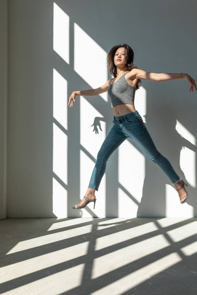 Asian dancer girl makes an acrobatic jump illuminated by the sun that enters through the window in an empty building. isolated - Φωτογραφία, εικόνα
