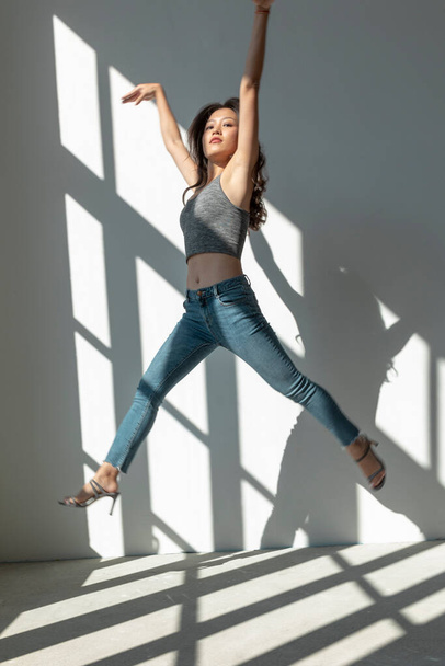 Asian dancer girl makes an acrobatic jump illuminated by the sun that enters through the window in an empty building. isolated - Foto, afbeelding