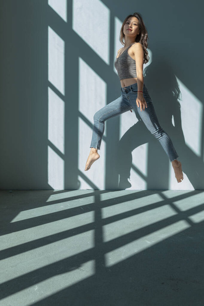 Asian dancer girl makes an acrobatic jump illuminated by the sun that enters through the window in an empty building. isolated - Foto, Imagem