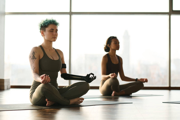 Young girls sitting in lotus position with eyes closed and meditating in health club - Foto, imagen