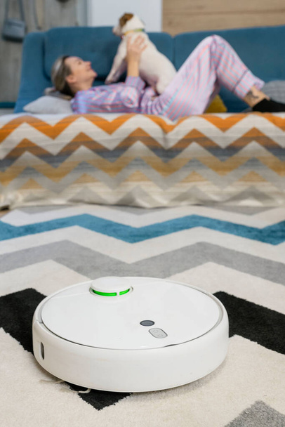 woman couple sitting on sofa with dogs cleaning floor using vacuum robot at home. - Photo, Image