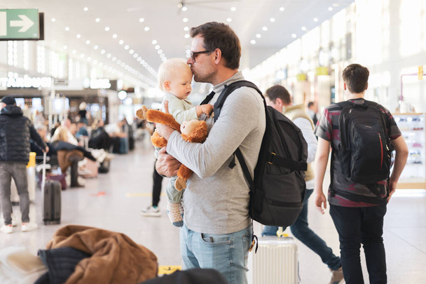 父は子供と一緒に旅行し、飛行機に乗るのを待っている空港ターミナルで幼児の男の子と抱き合ってキスをします。子供と一緒に旅行するコンセプト - 写真・画像