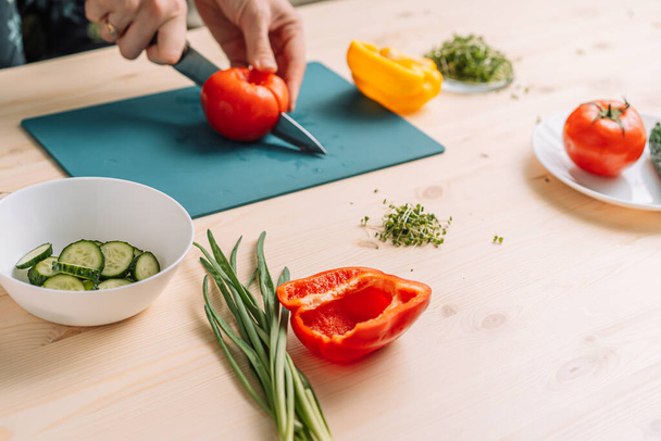 野菜サラダ用のトマトをマイクログリーンで切る女性. - 写真・画像