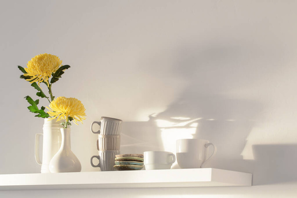 yellow chrysanthemum in vase and cups on white shelf on white background - Photo, image