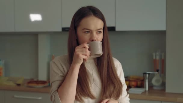 Primer plano de vídeo de la joven en la cocina bebiendo su taza de café de la mañana y sonriendo. - Metraje, vídeo