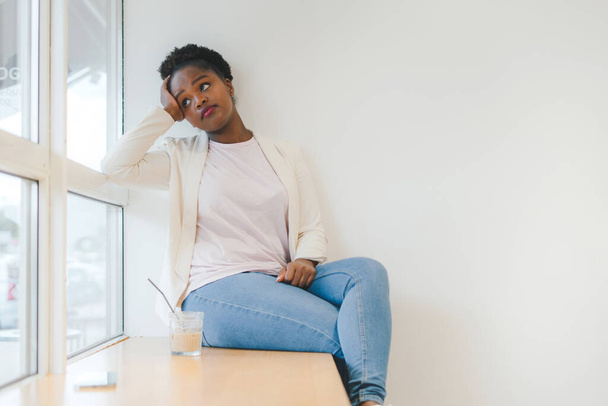 Przemyślana młoda Afroamerykanka, siedząca na stołówce i pijąca kawę, odwracając wzrok. Niezmieniony, styl życia i prosta koncepcja życia. - Zdjęcie, obraz