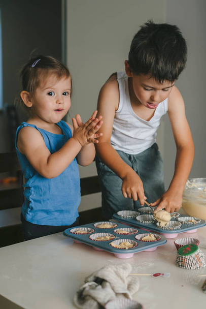 Little baby girl and boy learning to make cup cakes, pouring cake batter in cup cake moulds. Family education. Family concept. - Фото, зображення