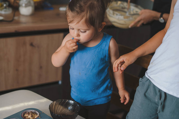 Cute little baby girl and her brother spooning muffin batter into the baking cups, baking at home. Family education. Family concept. - Fotó, kép