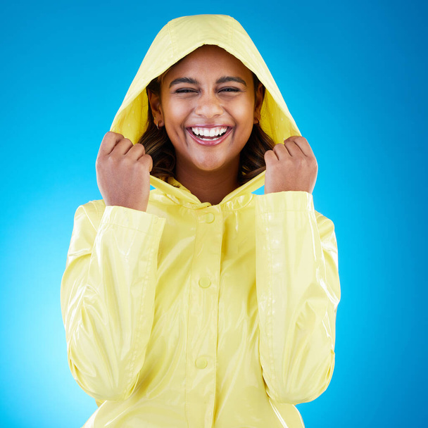 Capa, feliz e retrato de uma mulher com uma capa de chuva isolada em um fundo azul em um estúdio. Sorria, rindo e menina vestindo um casaco para proteger da chuva, o frio ou mau tempo em um pano de fundo. - Foto, Imagem