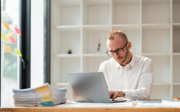 Jovem homem de negócios usando óculos usando laptop, digitando no teclado, escrevendo e-mail ou mensagem, sentado no escritório. - Foto, Imagem
