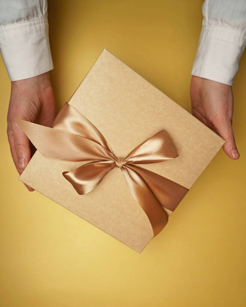 On a yellow flat background hands hold a gift - Foto, imagen