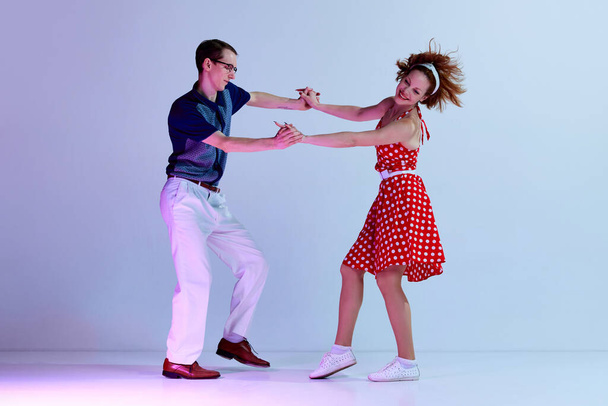 Positive energy. Young girl and man in colorful costumes dancing social dances against gradient blue purple studio background. Concept of art, retro style, party, fun, movements, 60s, 70s culture - Foto, imagen