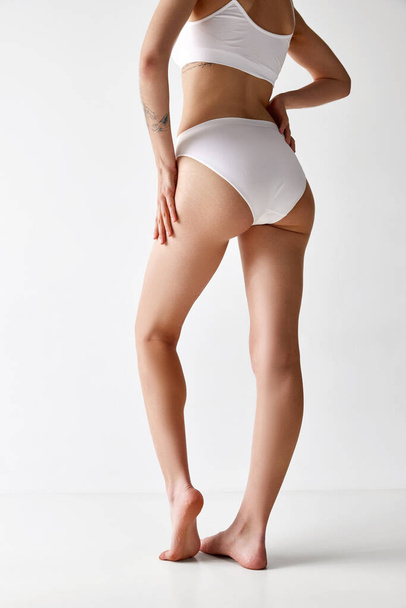 Cropped image of slender young woman with sportive body shape in cotton inner wear over white background. Concept of skin care, sport, fitness, dieting and anti-cellulite program, ad. Rear view - 写真・画像
