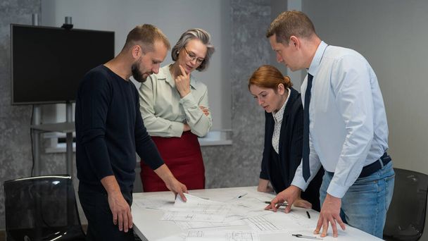 Four business people review and discuss blueprints. Designers engineers at a meeting - Fotografie, Obrázek