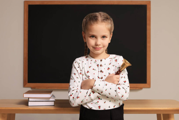Pupil with school bell near desk and chalkboard in classroom - Foto, Bild