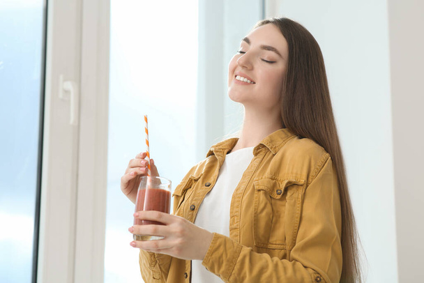 Beautiful young woman with delicious smoothie near window indoors. Space for text - Foto, afbeelding