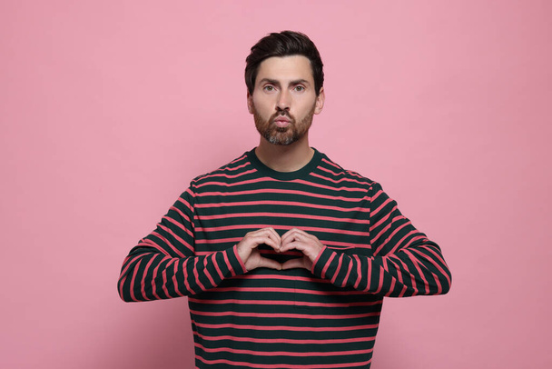 Handsome man making heart with hands and blowing kiss on pink background - 写真・画像