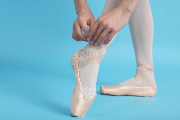 Young ballerina tying pointe shoes on light blue background, closeup - 写真・画像