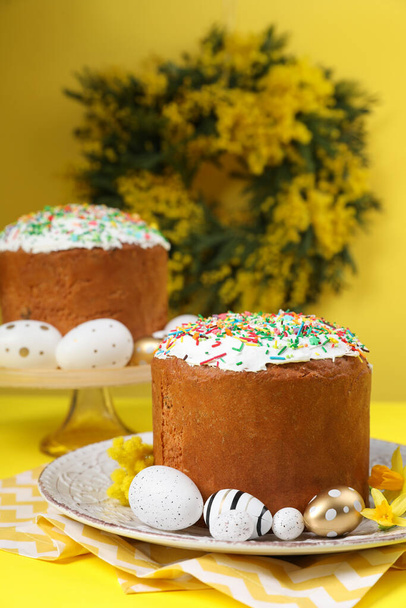 Traditional Easter cakes with sprinkles, painted eggs and beautiful spring flowers on yellow background - Photo, image