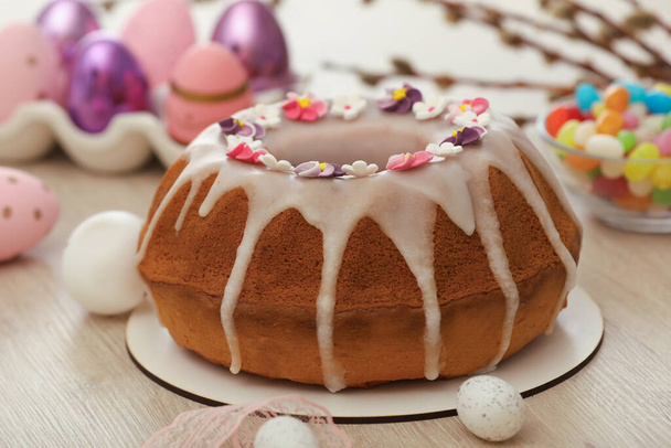 Délicieux gâteau de Pâques décoré d'aspersions près des œufs peints sur une table en bois blanc, gros plan - Photo, image