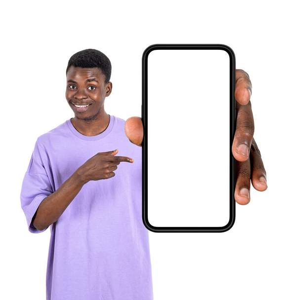 Black smiling man finger pointing at smartphone in hand, isolated over white background. Concept of mobile app and social network. Mock up copy space display - Fotoğraf, Görsel