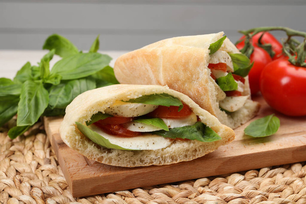 Delicious pita sandwiches with mozzarella, tomatoes and basil on wicker mat - Фото, изображение