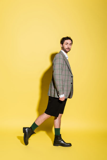 Full length of trendy model in shorts and jacket standing on yellow background  - Photo, Image