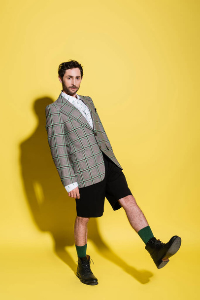 Full length of trendy model in jacket and shorts standing on yellow background with shadow  - Fotó, kép