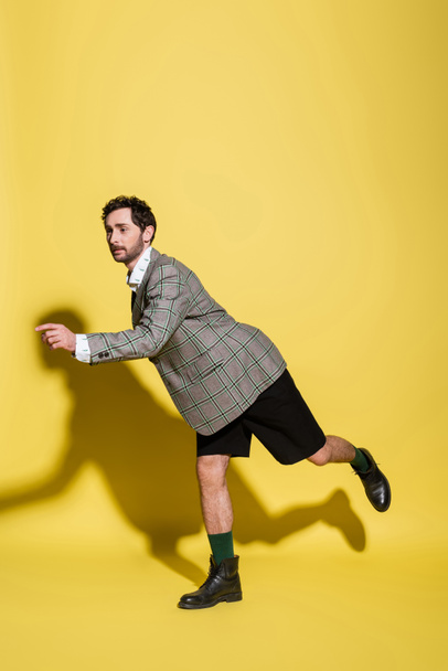 Fashionable model in shorts and plaid jacket posing on yellow background  - Zdjęcie, obraz